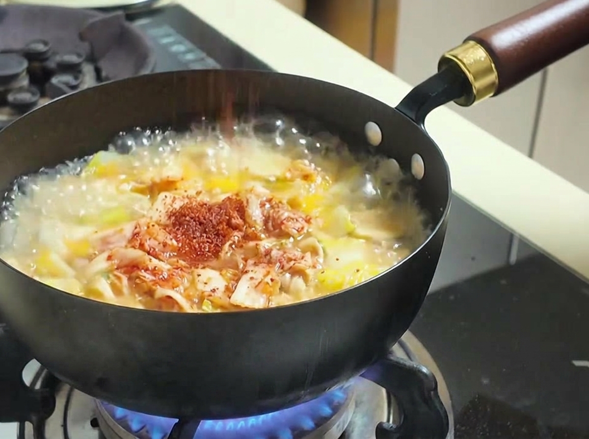 Czerwona papryka chili w proszku sypana do gotującej się zupy z kimchi i warzywami.