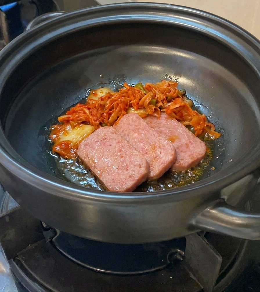 Posiekane kimchi dodawane do garnka z częściowo podsmażonymi kawałkami mięsa.
