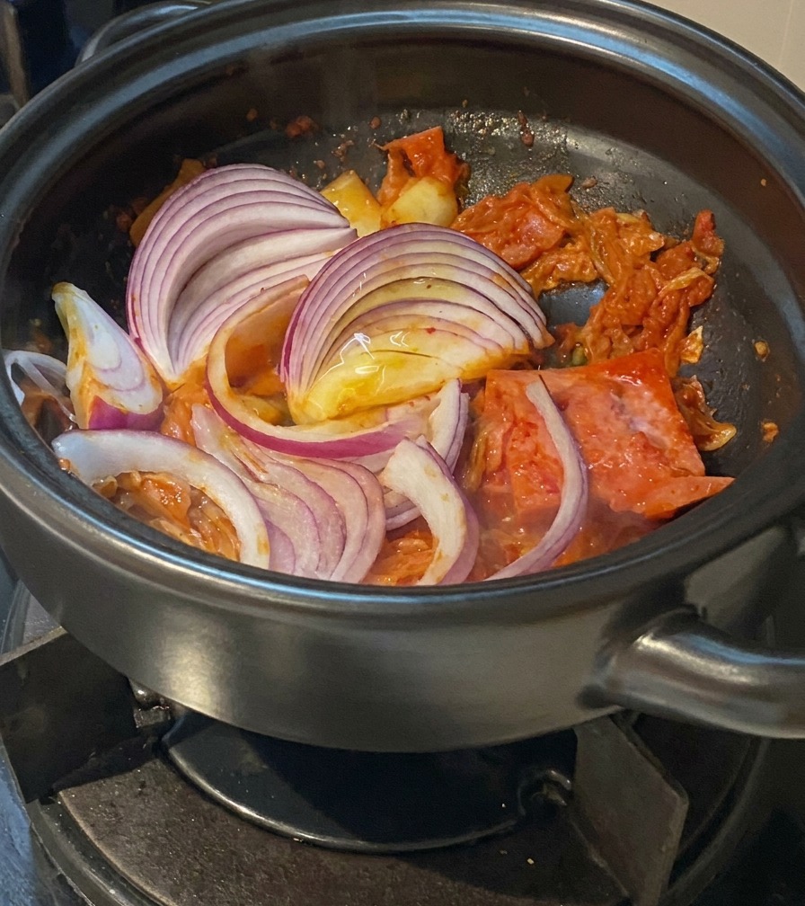 Piórka czerwonej cebuli mieszane z podsmażanym kimchi i boczkiem w garnku.