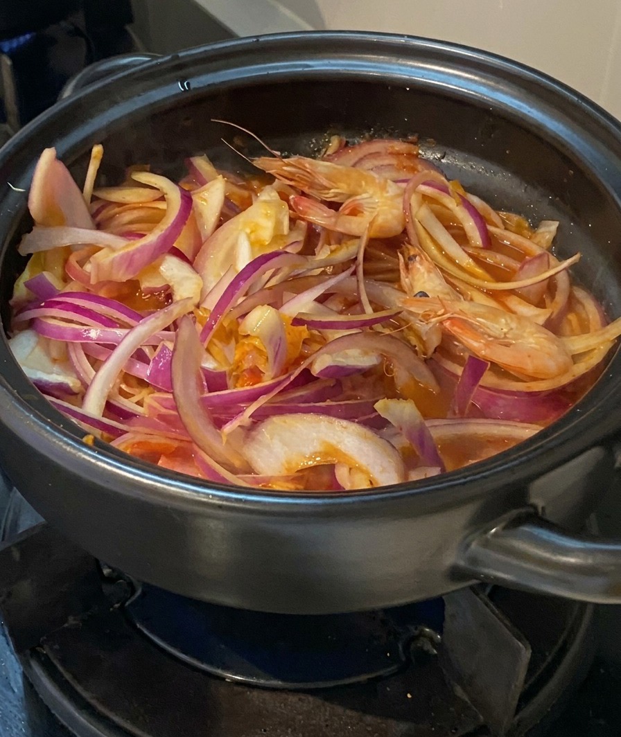 Świeże całe krewetki z głowami dodawane do garnka z cebulą, kimchi i boczkiem.