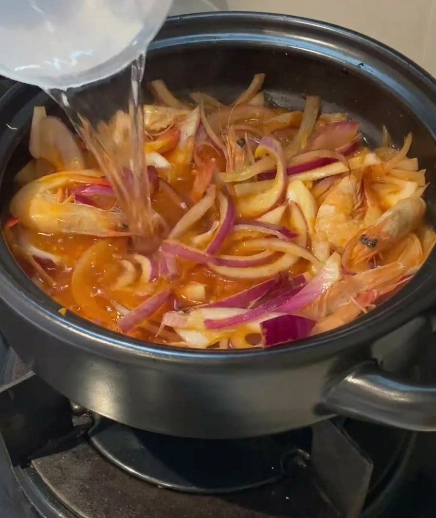 Czysta woda wlewana z pojemnika do ceramicznego garnka wypełnionego krewetkami, cebulą i kimchi.