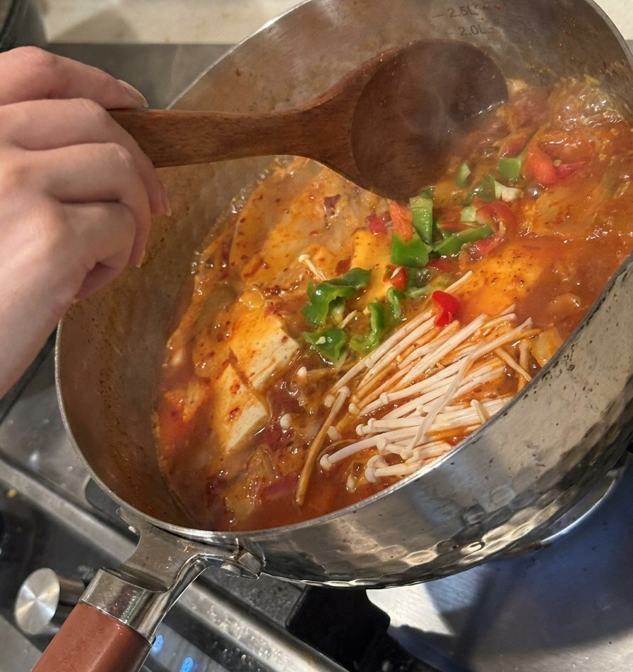 Pokrojona zielona papryka i sfermentowane kimchi dodawane do gotującej się zupy.