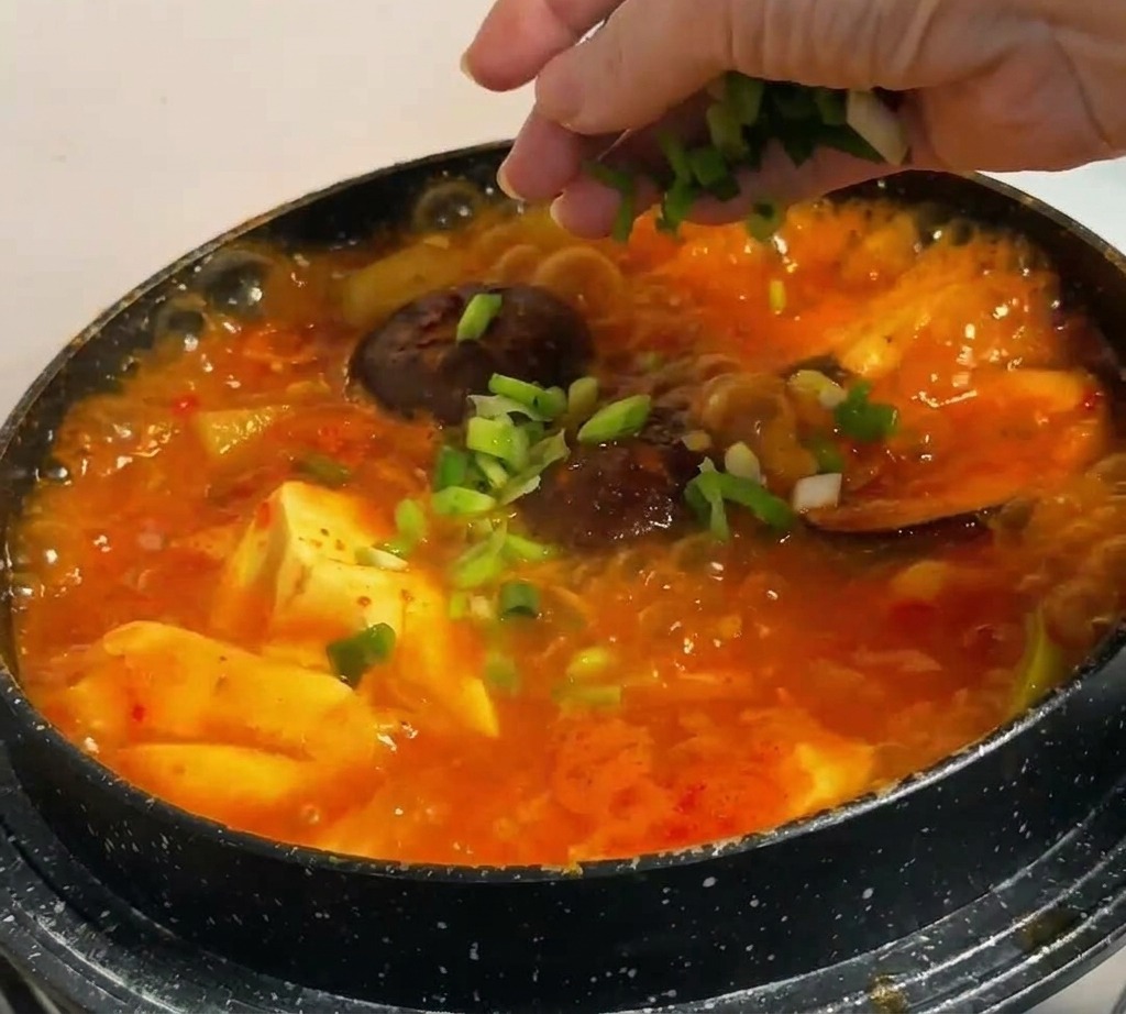 Posypywanie bulgoczącej, czerwonej zupy świeżą dymką i plastrami chili.