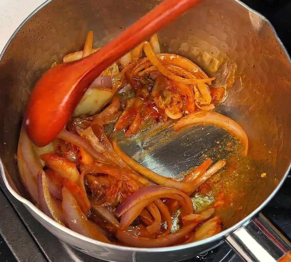 Mieszanie posiekanego kimchi i cebuli drewnianą łyżką w garnku.
