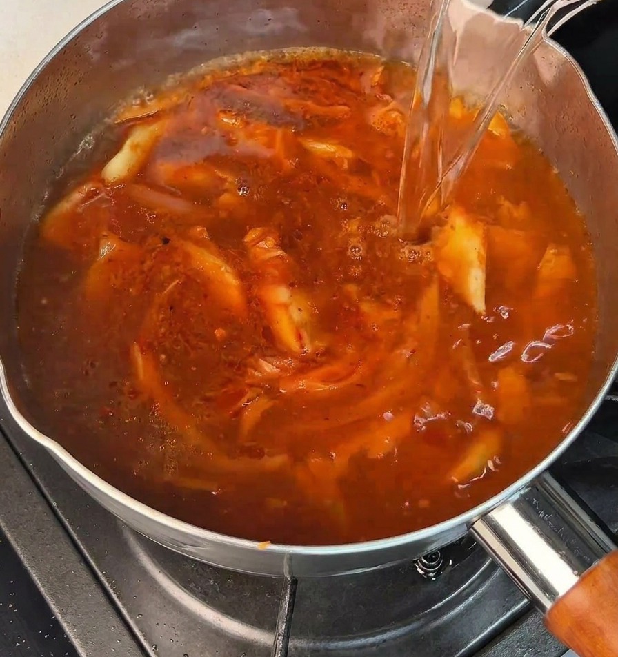 Wlewanie wrzącej wody do garnka z bąbelkującą czerwoną bazą.