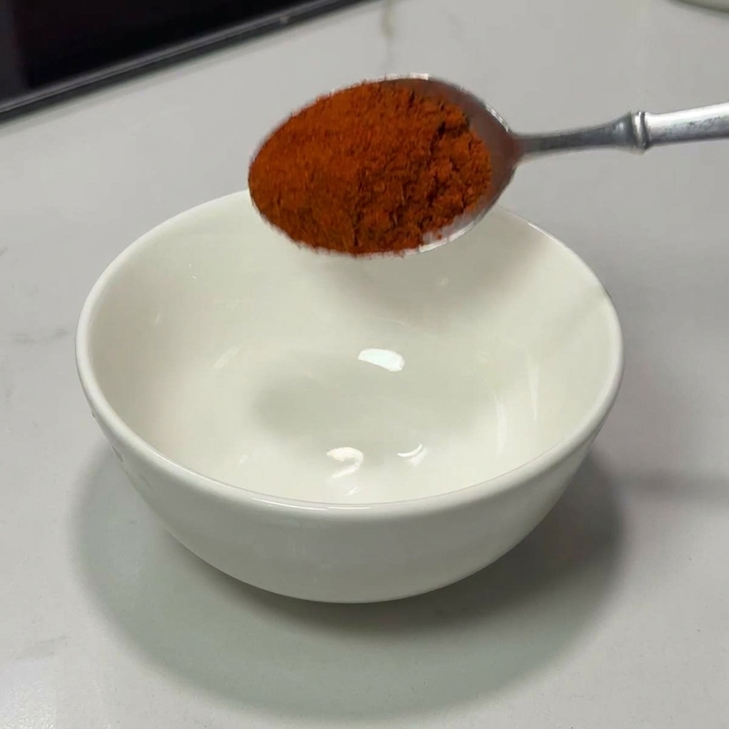 Srebrna łyżka wsypująca czerwoną paprykę chili do białej miseczki ceramicznej.