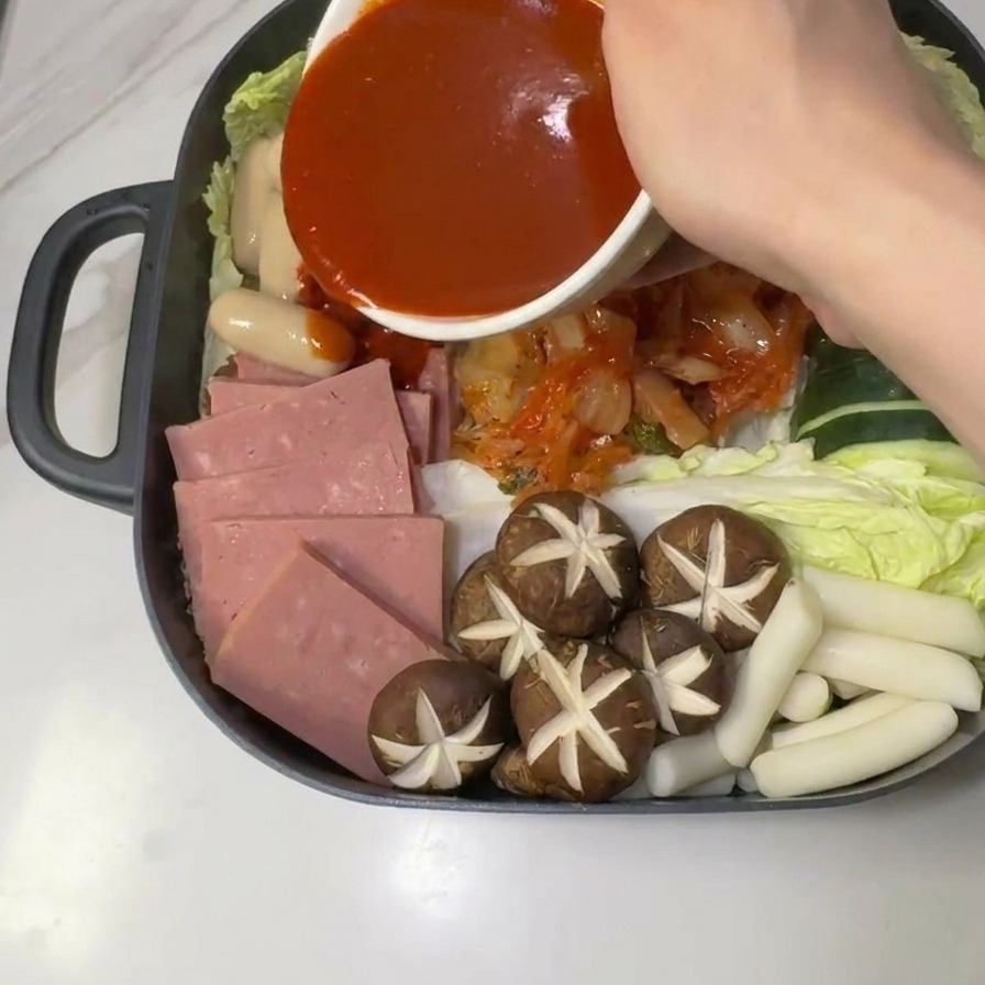 Czerwony sos gochujang wylewany z miseczki na środek surowych składników zupy armijnej.