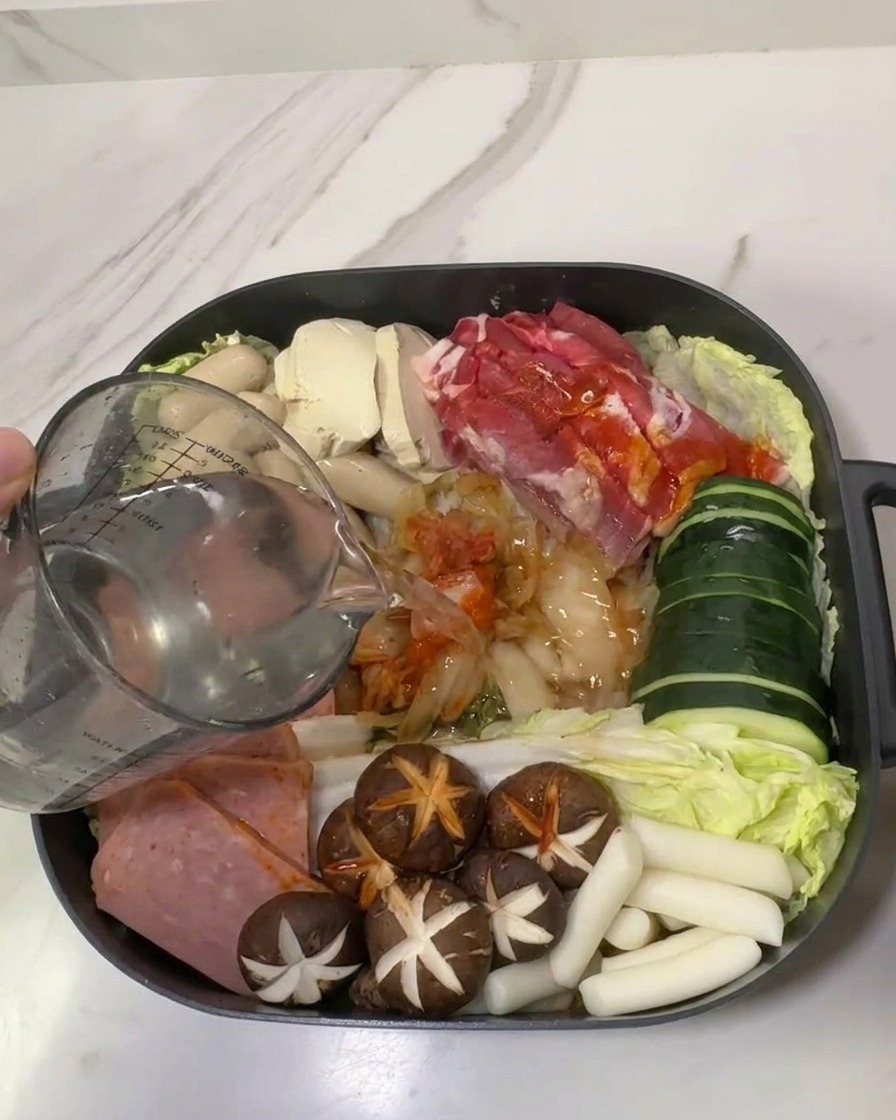 Woda wlewana z miarki do garnka wypełnionego składnikami na Budae Jjigae.