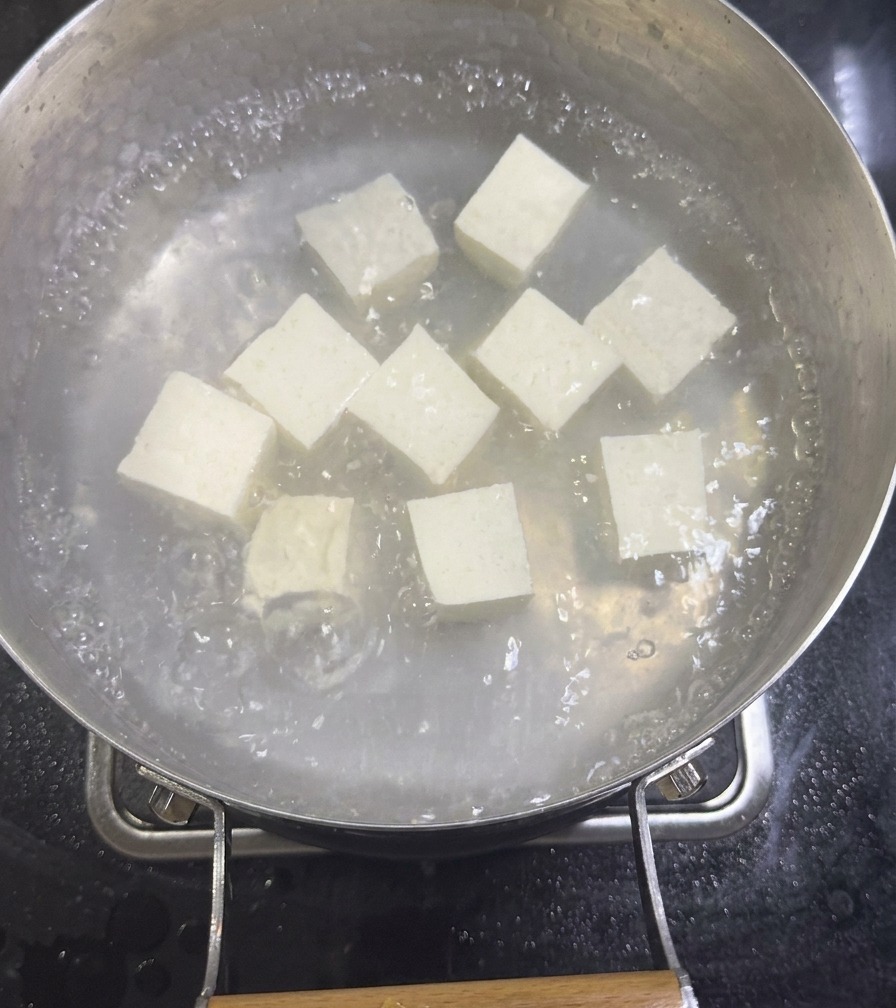 Kostki białego jedwabistego tofu gotujące się w garnku z rozcieńczonym bulionem z małży na kuchence.