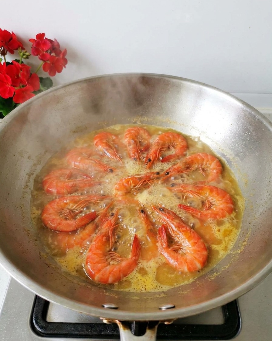 Pomarańczowe krewetki gotujące się w jasnym bulionie w woku, widoczna para.