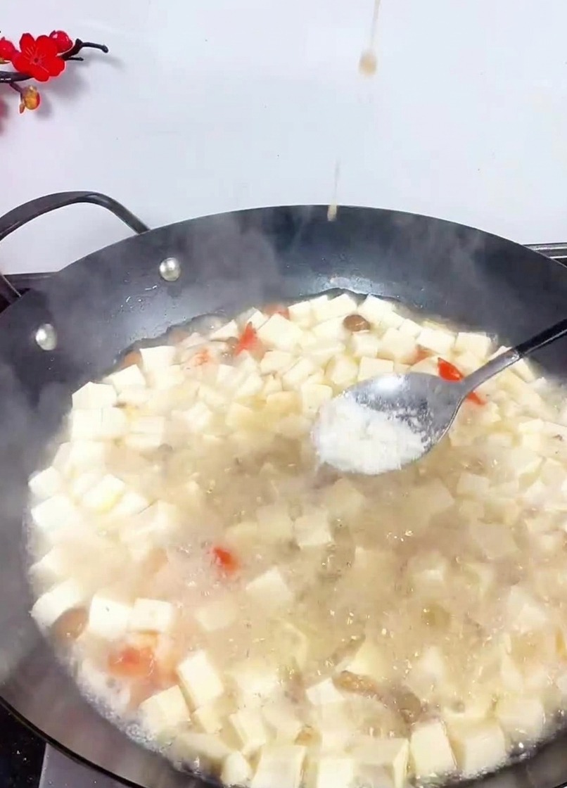 Łyżka sypiąca sól do woka z gotującą się zupą i kostkami tofu.