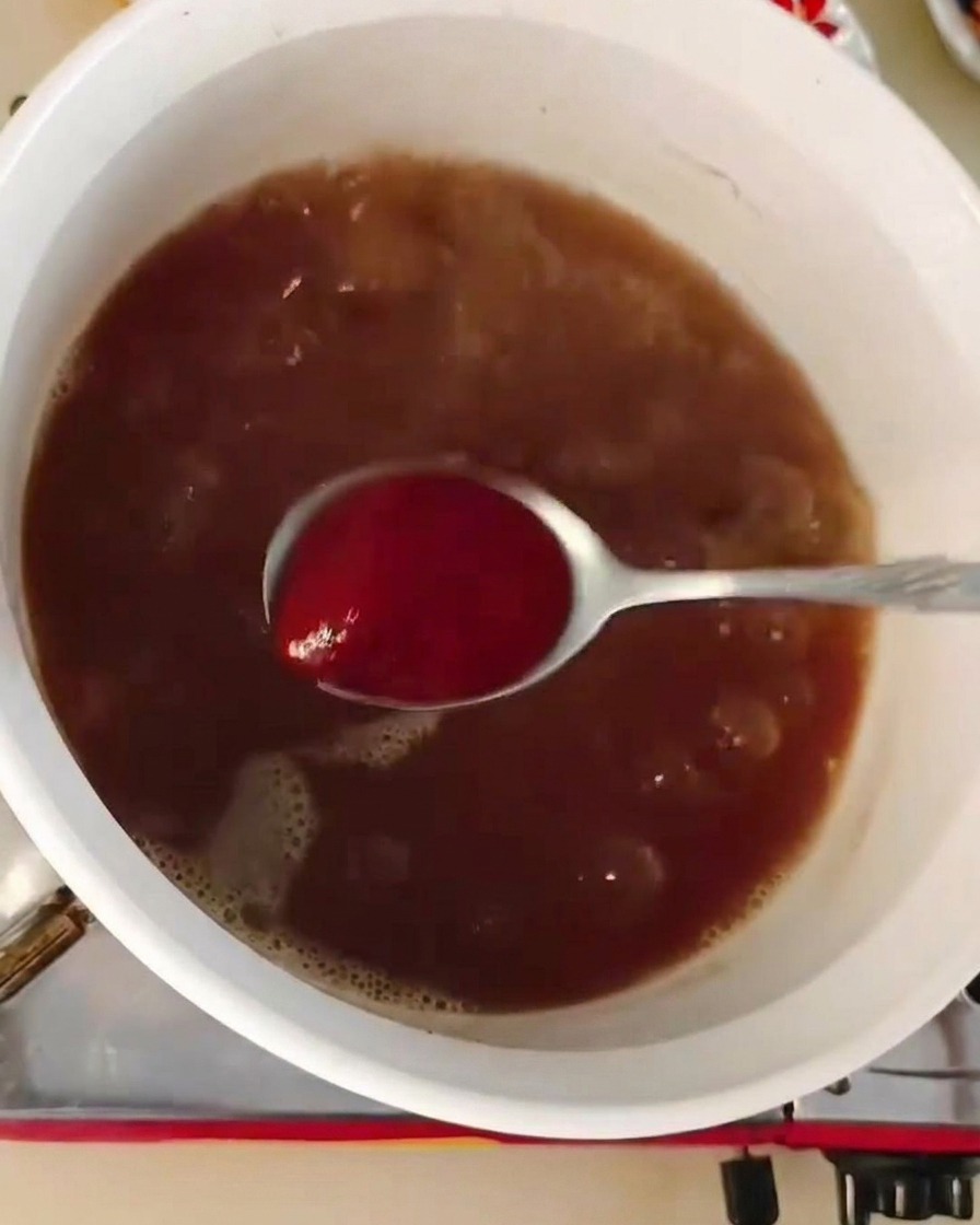 Mieszanie łyżki czerwonej pasty chili w gotującej się bazie zupy o ciemnobrązowym kolorze.