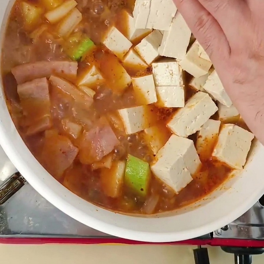 Wkładanie kostek świeżego białego tofu do garnka z gotującą się zupą koreańską.