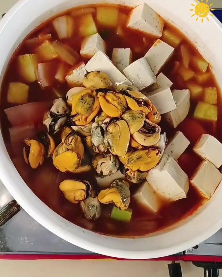 Mięso omułków i surowe krewetki dodawane do gotującego się kociołka z tofu i warzywami.