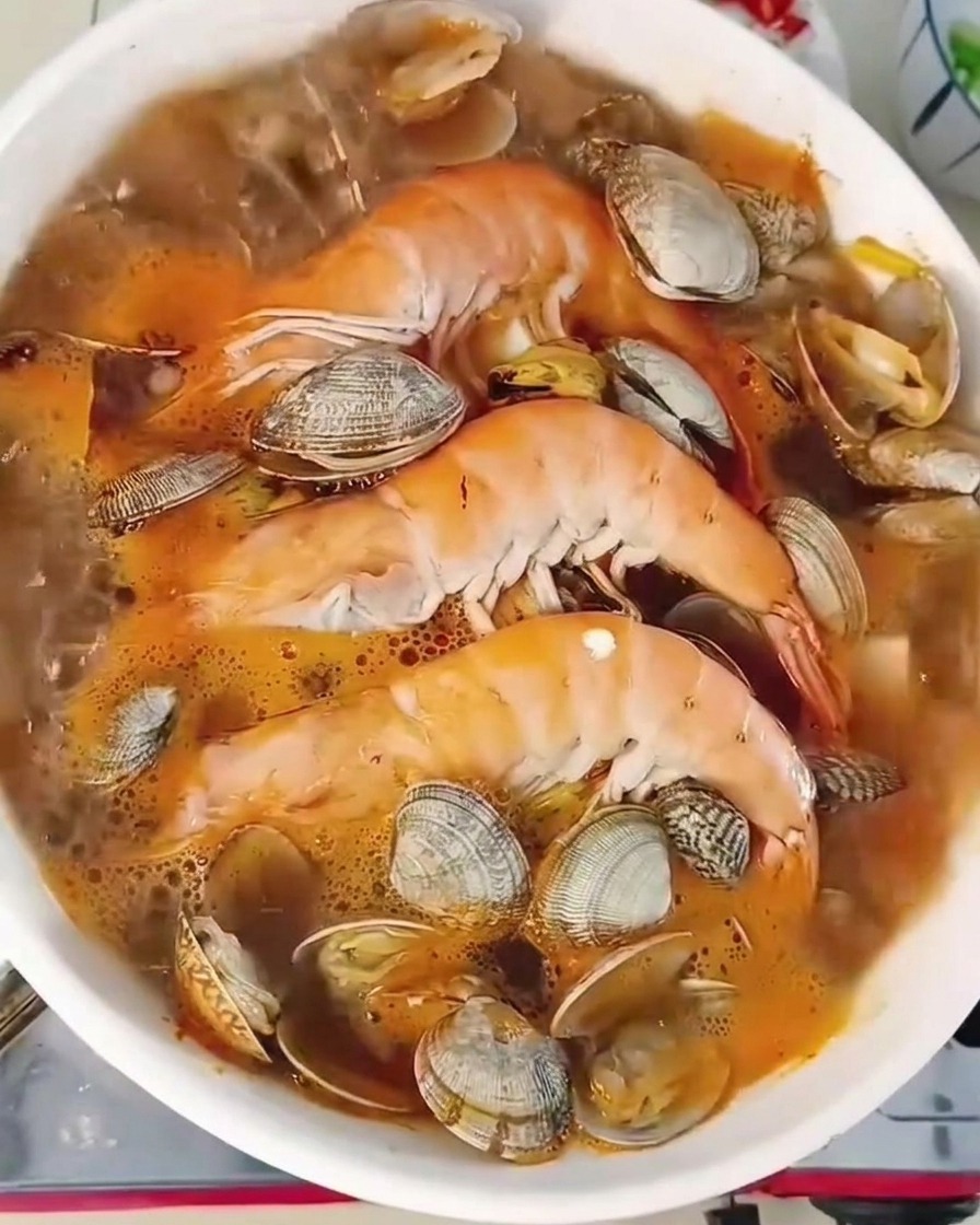 Zbliżenie na gotującą się zupę z krewetkami i tofu, posypaną świeżą dymką i papryczkami chili.