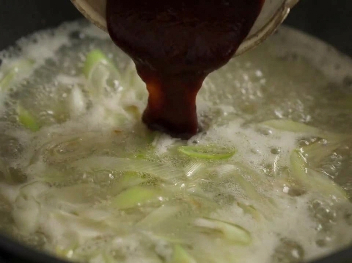Duża łyżka ciemnoczerwonej pasty chili dodawana do wrzącego bulionu z warzywami.