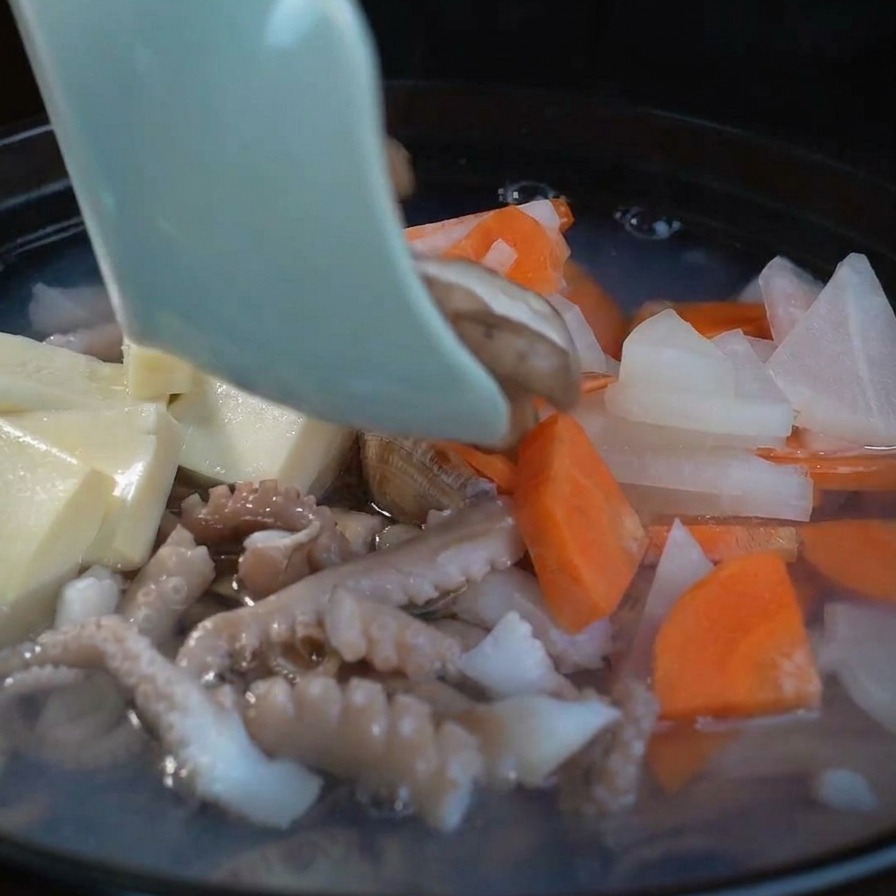 Plastry świeżych grzybów shiitake dodawane do bulgoczącej zupy obok tofu i warzyw.