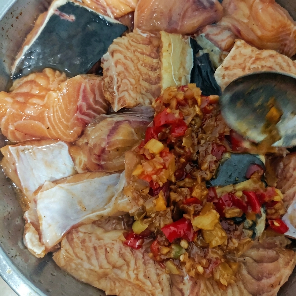 Metalowy talerz z surową rybą pokrywany łyżką gęstym, grudkowatym sosem z chili i czosnku.