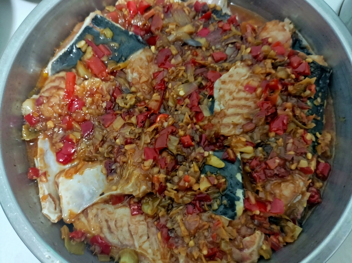 Stalowa taca parowaru wypełniona kawałkami ryby z jaskrawym czerwonym sosem z siekanego chili.