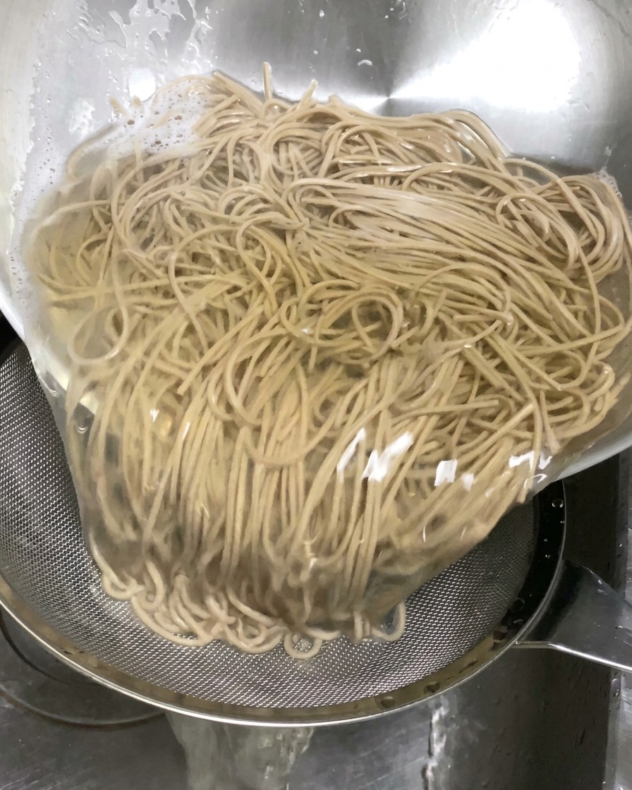 Ugotowany makaron soba przelewany z dużej miski na metalowe sito umieszczone w zlewie.