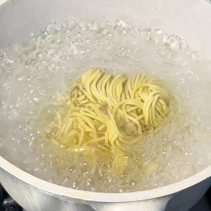 Porcja żółtego japońskiego makaronu ramen gotująca się w garnku z mocno wrzącą wodą.