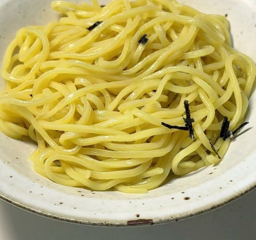 Biała ceramiczna miska z żółtym makaronem ramen posypanym paskami czarnych wodorostów nori.
