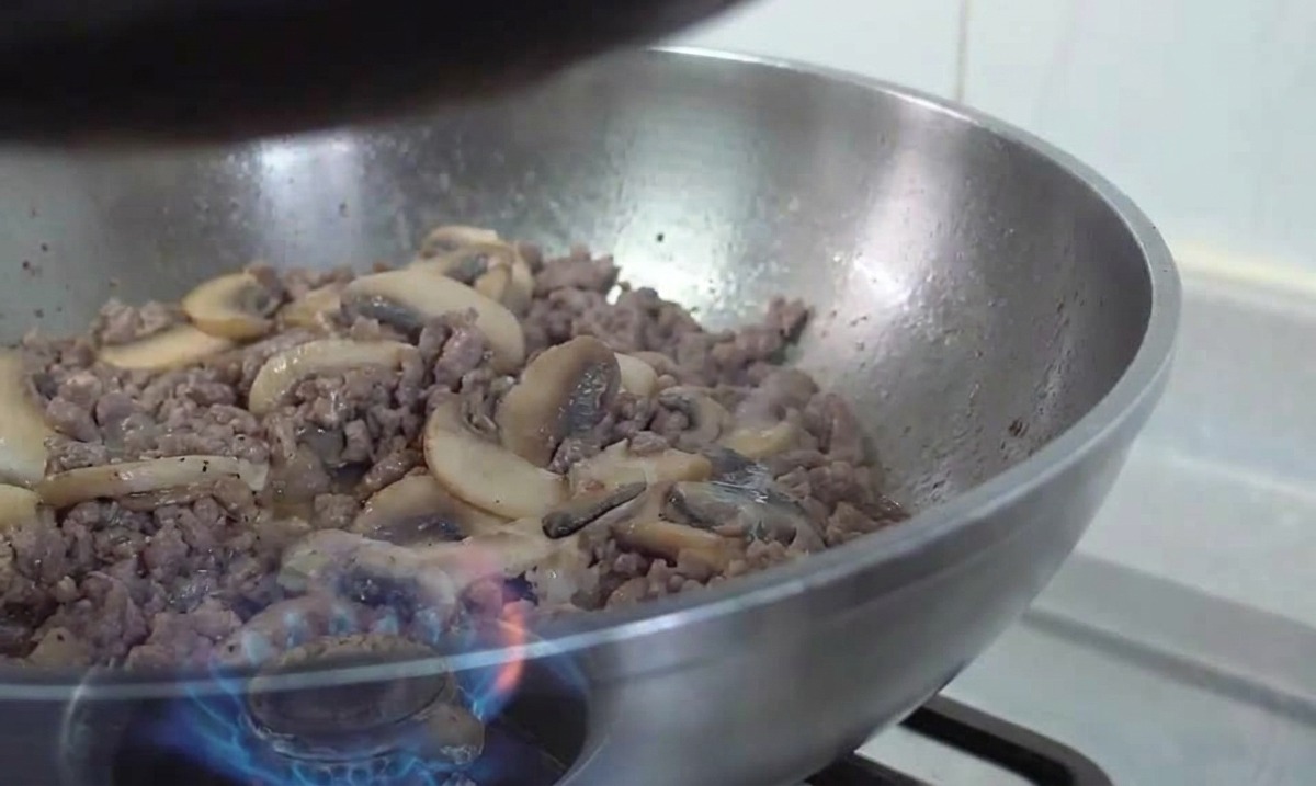 Stalowy wok z mieszanką zrumienionej wołowiny i podsmażonych pieczarek podrzucaną nad płomieniem gazowym.