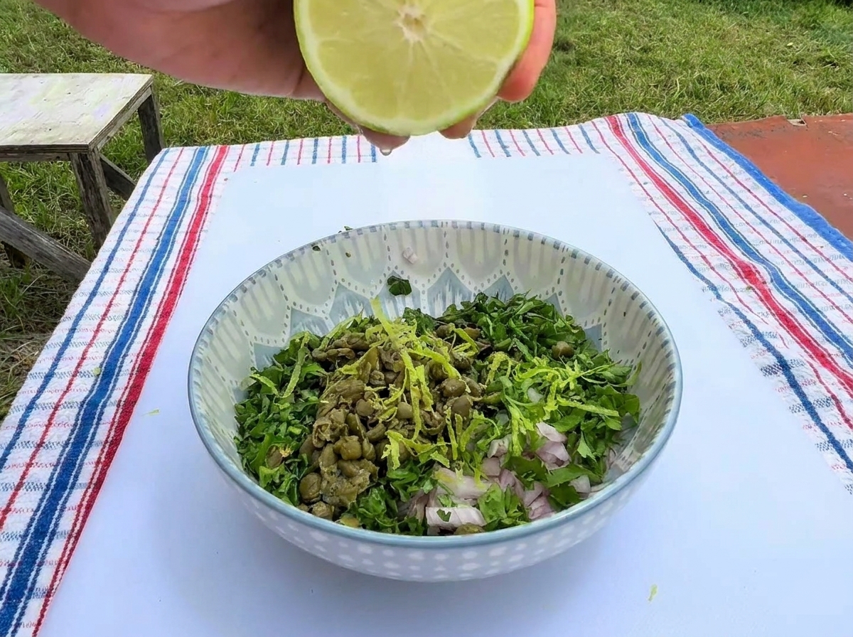 Ręka wyciskająca połówkę limonki do miseczki z posiekanymi ziołami, kaparami i szalotką.