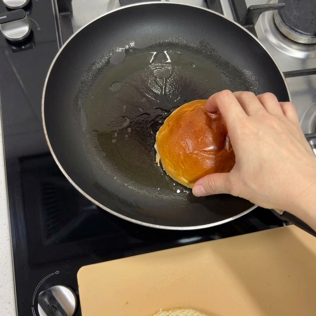 Dłoń kładąca bułkę brioche na rozgrzaną patelnię w celu jej zarumienienia.