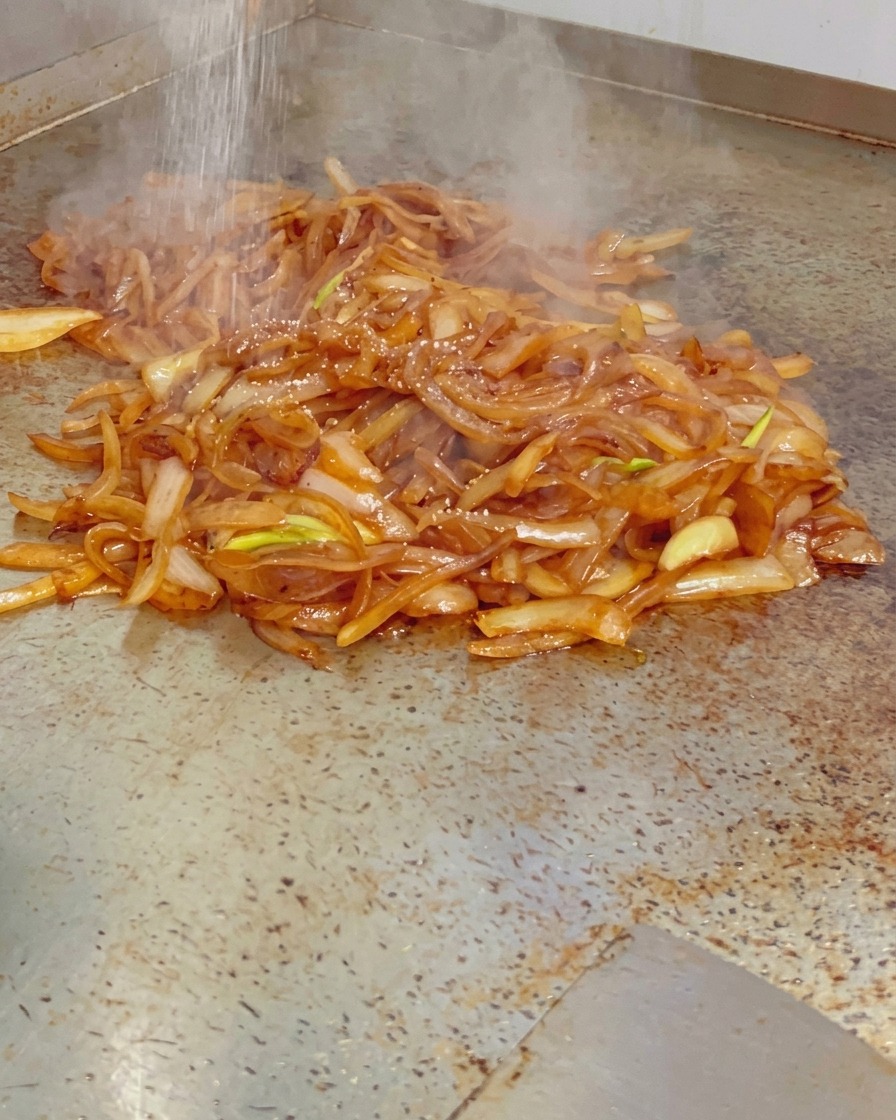Drobna sól sypana na stos parującej, lśniącej cebuli karmelizowanej na gorącym grillu.