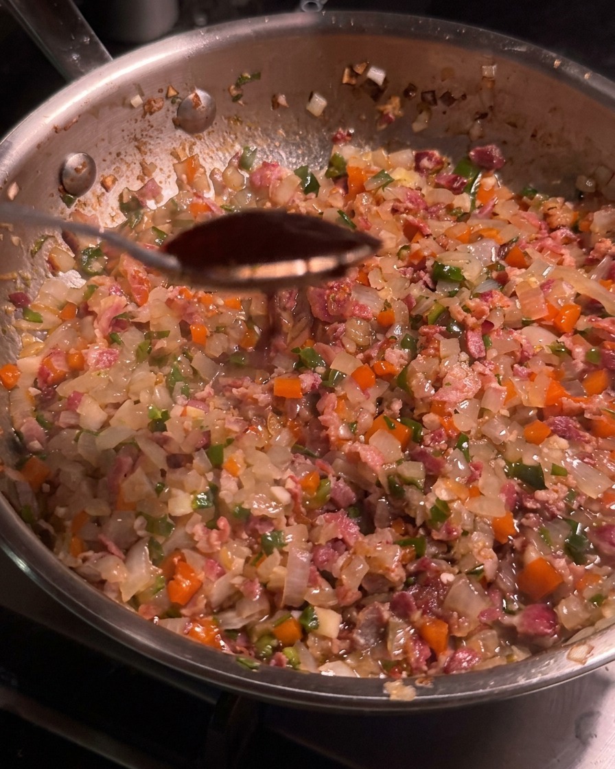 Łyżka ciemnego sosu chipotle nad patelnią wypełnioną boczkiem i warzywami.