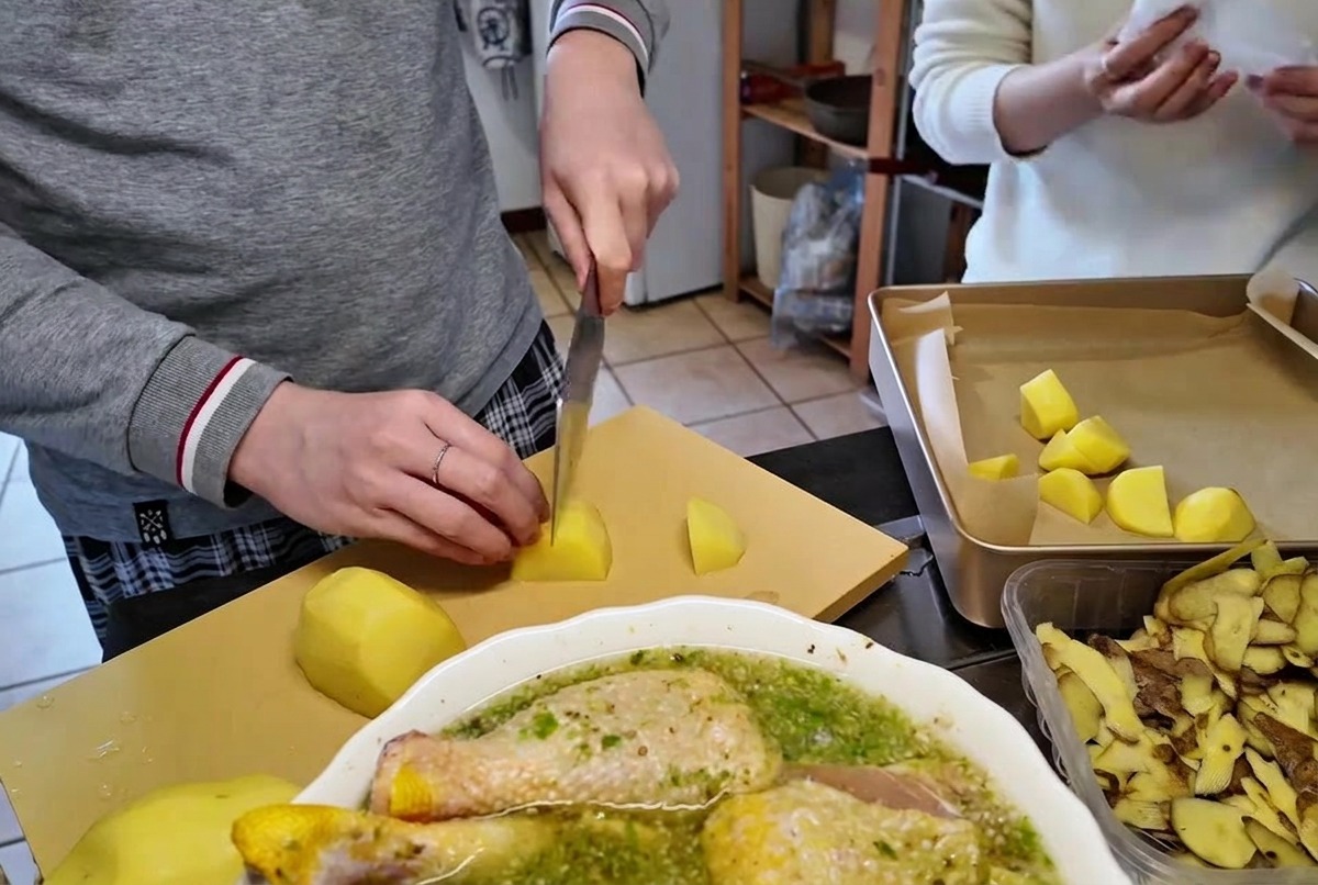 Krojenie obranych surowych ziemniaków na kawałki wielkości kęsa na desce do krojenia za pomocą ostrego noża kuchennego.