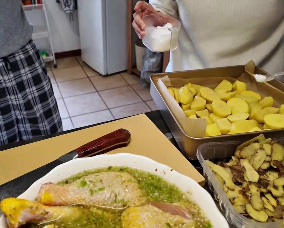 Kawałki surowych ziemniaków ułożone na blasze wyłożonej papierem do pieczenia, posypywane solą z przezroczystego pojemnika.