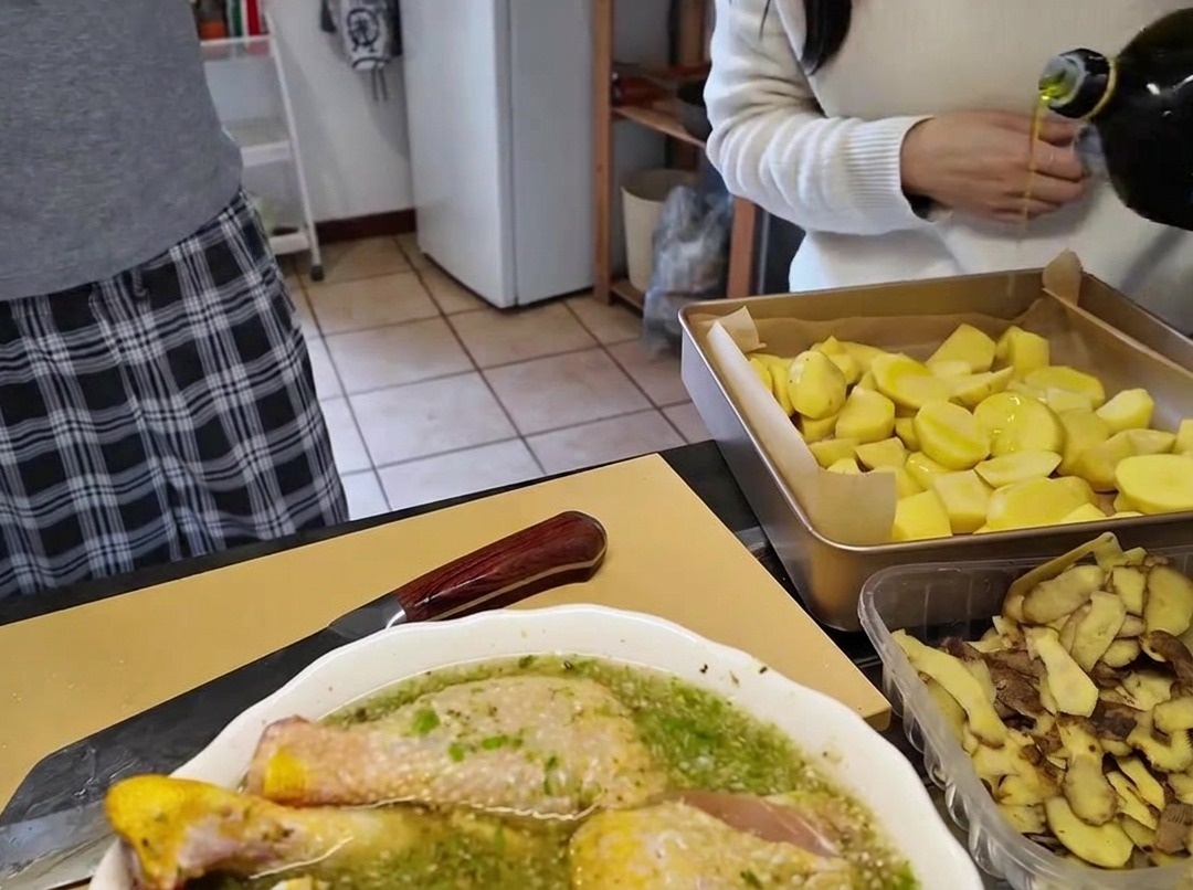 Wlewanie oliwy z oliwek z szklanej butelki na blachę do pieczenia pełną pokrojonych kawałków ziemniaków.
