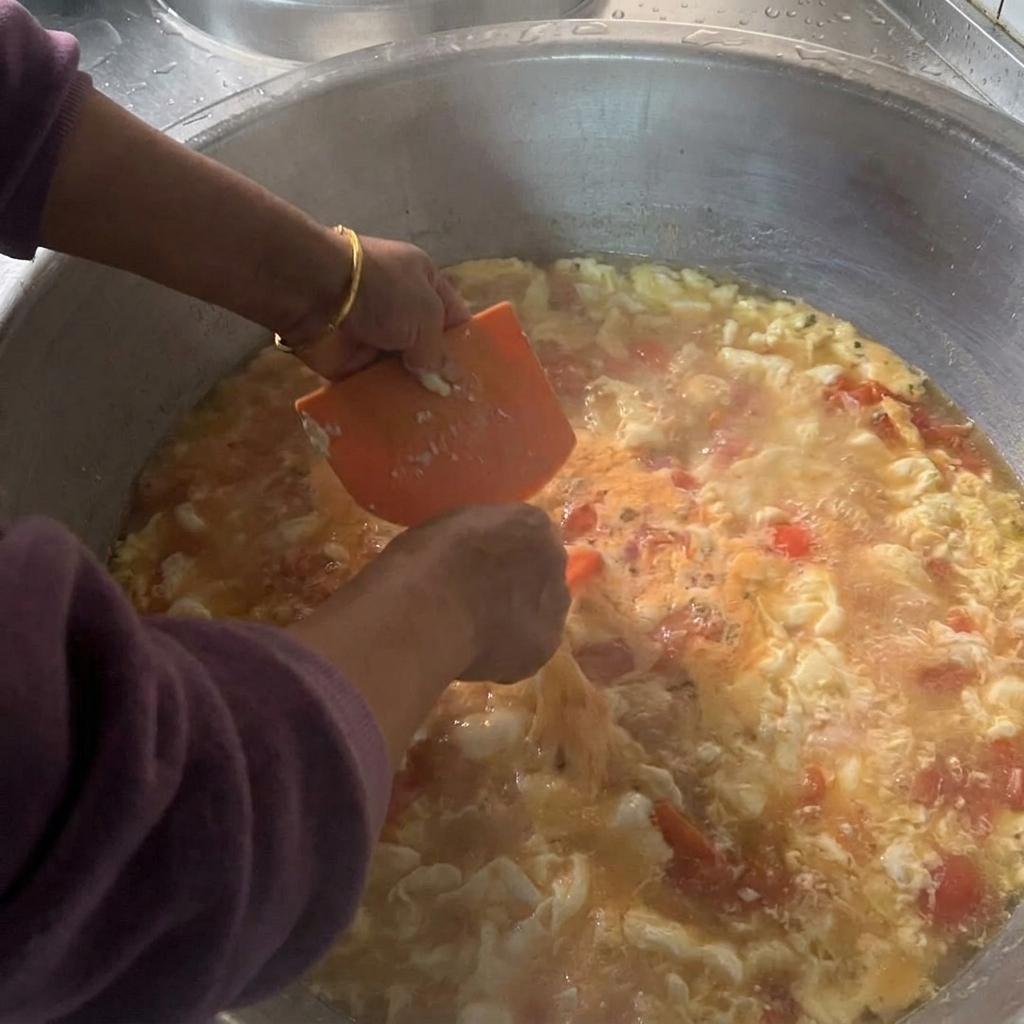 Dłonie trzymające pomarańczową plastikową skrobaczkę, za pomocą której odcinane są małe kawałki mokrego ciasta wprost do garnka z wrzącą zupą.