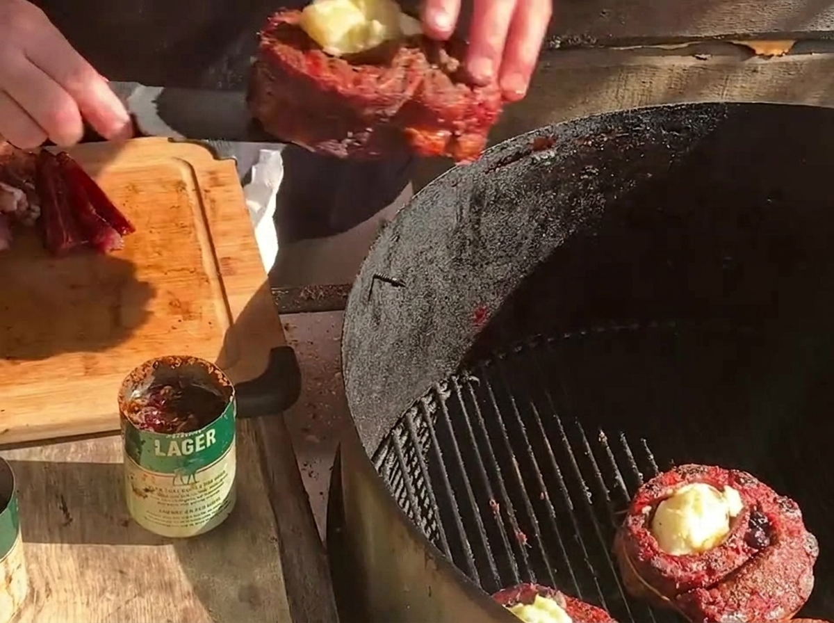 Umieszczanie na grillu węglowym faszerowanego koszyczka obok drugiego mięsa i grubych plastrów boczku.