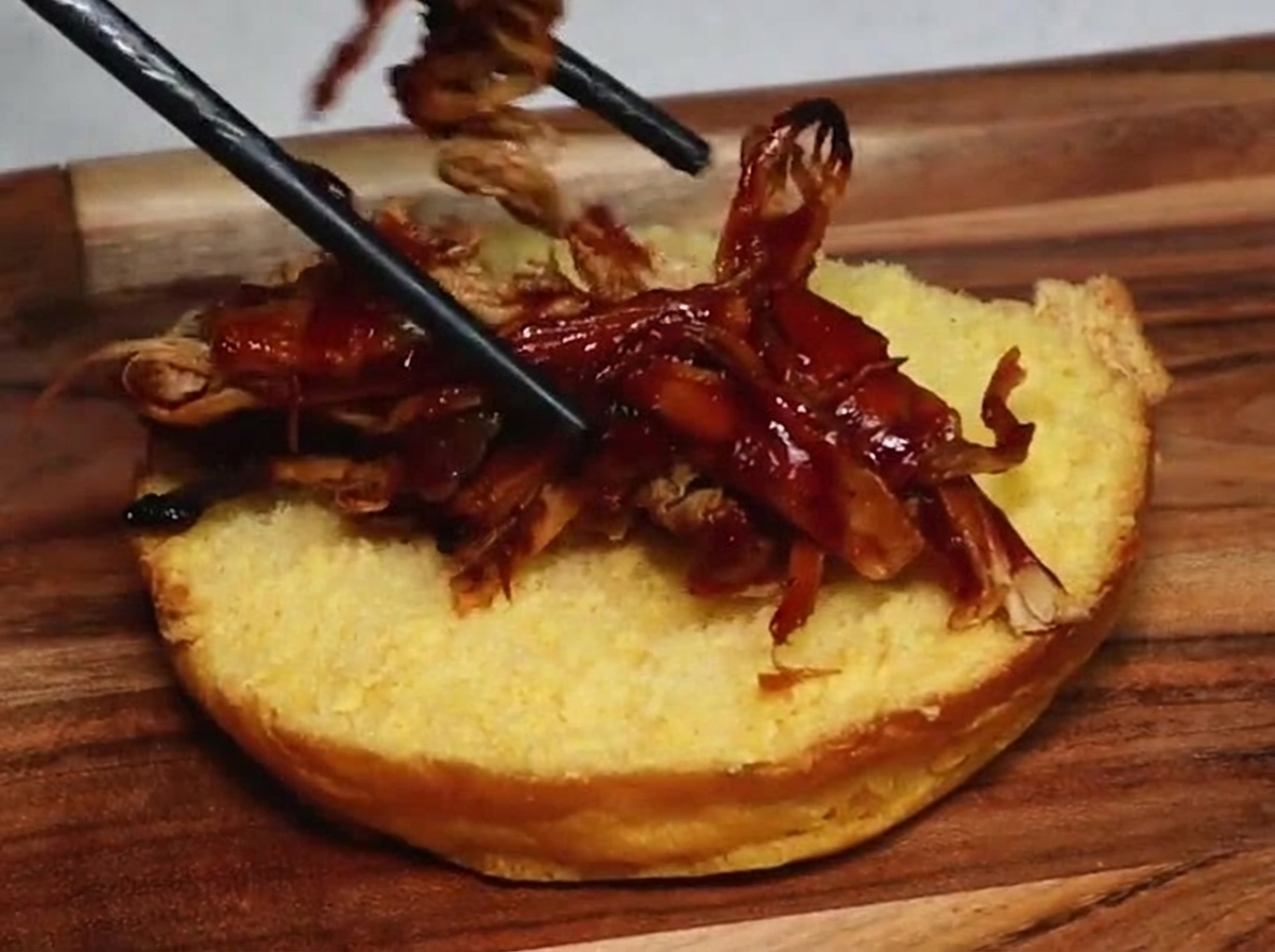 Pałeczki nakładające soczystą szarpaną wieprzowinę pokrytą gęstym sosem barbecue na opieczoną, dolną połowę bułki.