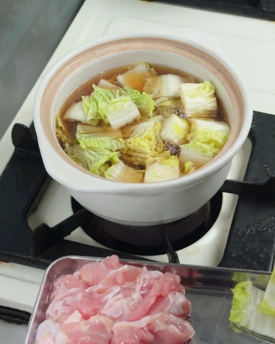 Posiekana kapusta pak choi gotująca się w bulionie pod przykryciem.