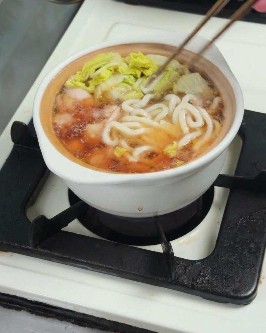 Makaron udon dodawany do garnka z bulionem, kurczakiem i kapustą.