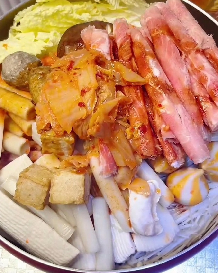 Kopczyk posiekanego czerwonego kimchi dodawany do garnka, do którego wlewana jest woda.