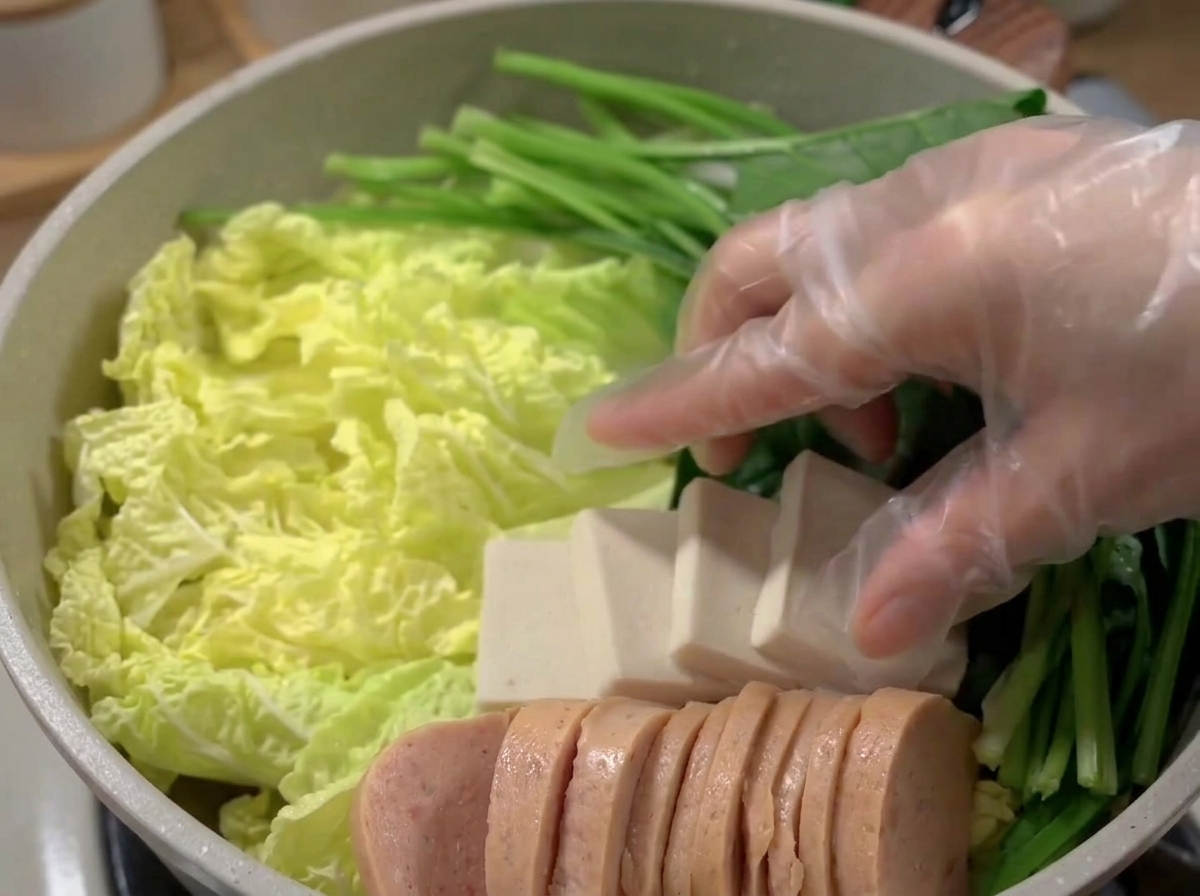 Szeroki garnek wypełniony pięknie ułożonymi warstwami mielonki, tofu, ciastek rybnych i warzyw.
