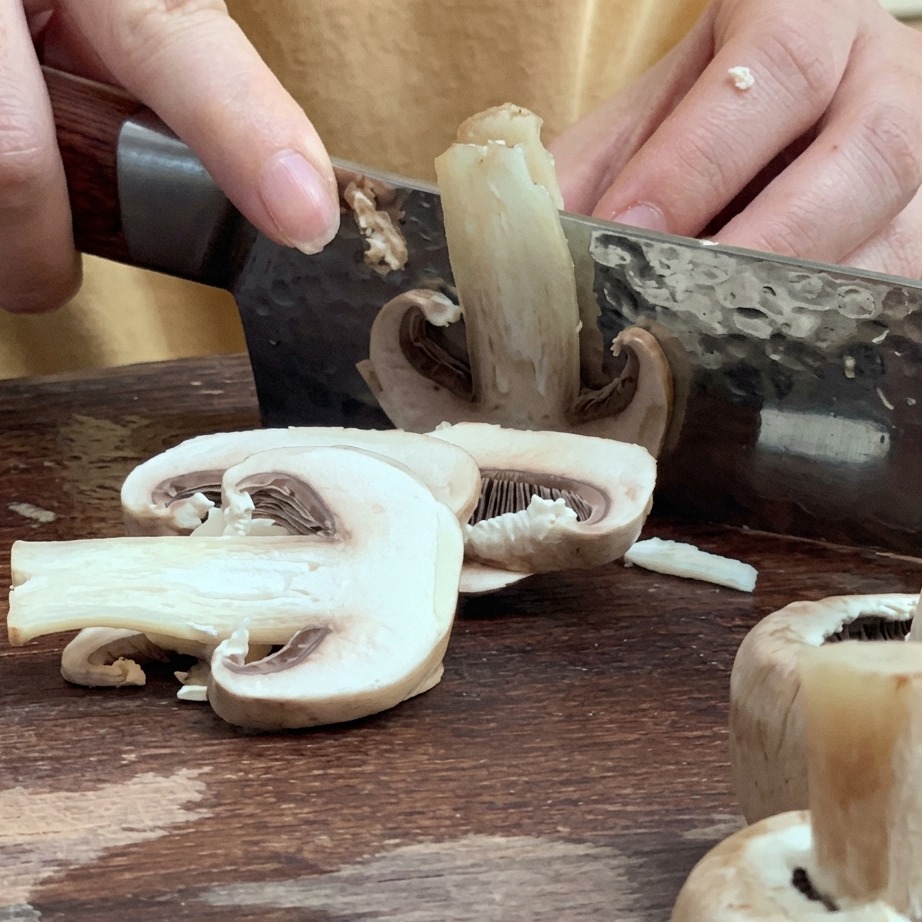 Świeże pieczarki krojone w cienkie plasterki na desce do krojenia.