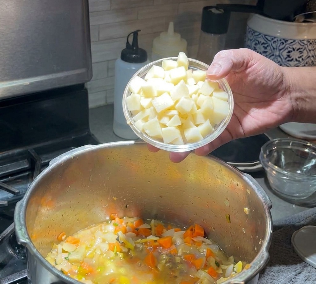Ręka wsypująca pokrojone ziemniaki do garnka z zupą.