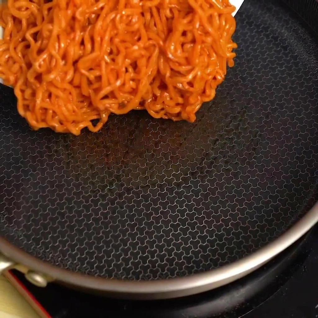 Ugotowany pikantny makaron wylewany z miski na gorącą, czarną patelnię.