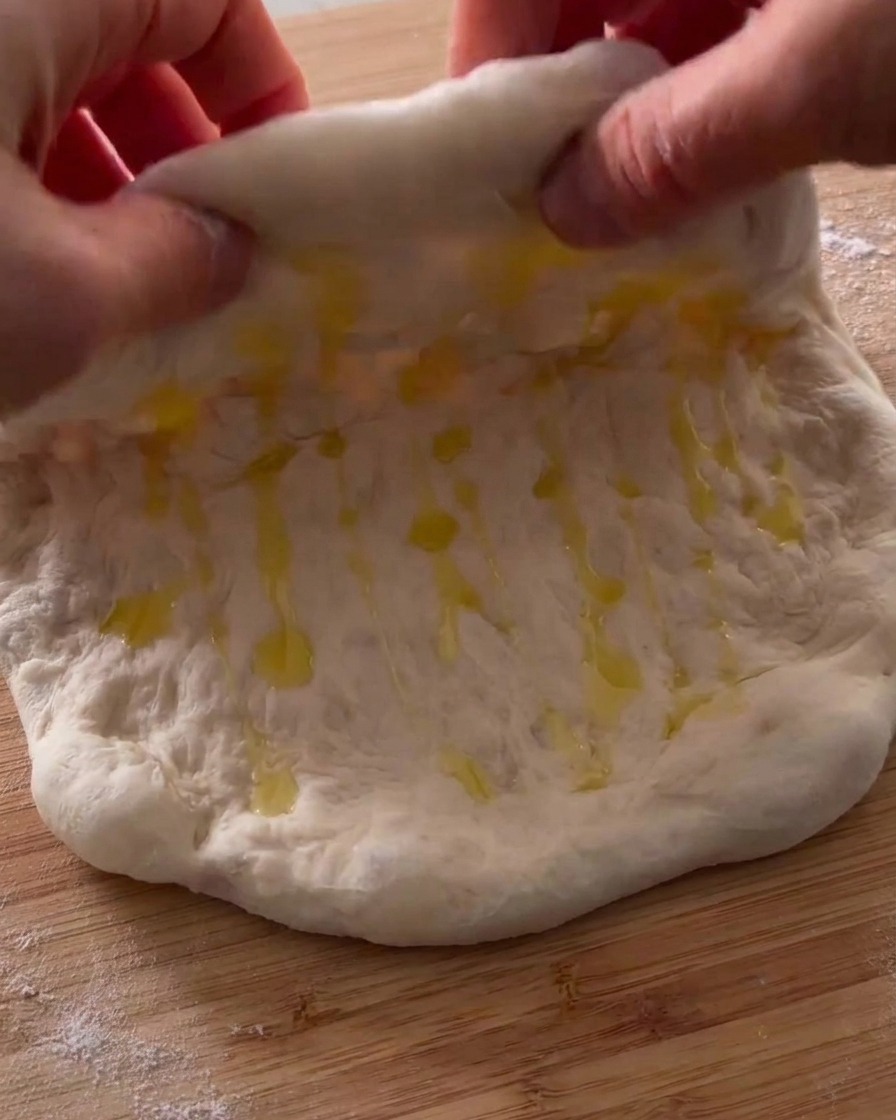Dłonie składające naoliwione ciasto do pizzy na pół.