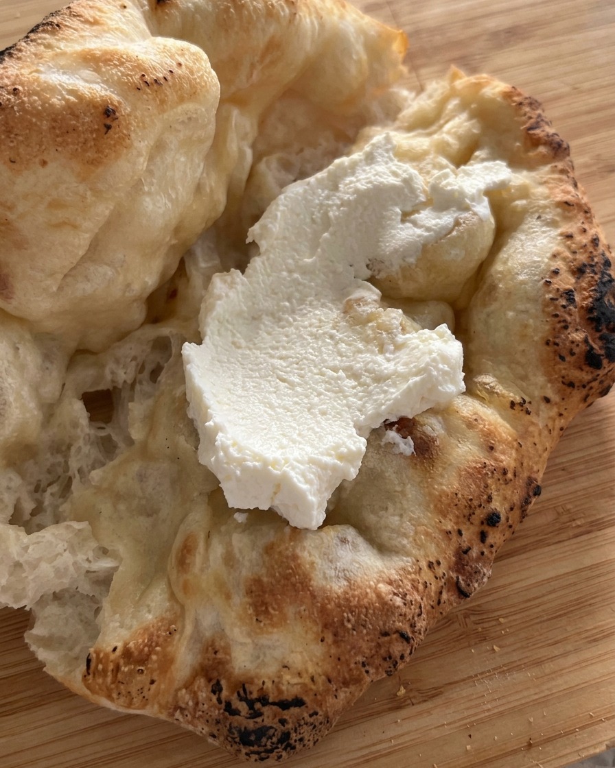 Gruba warstwa białego sera ricotta rozprowadzona wewnątrz świeżo upieczonego chlebka z ciasta do pizzy.