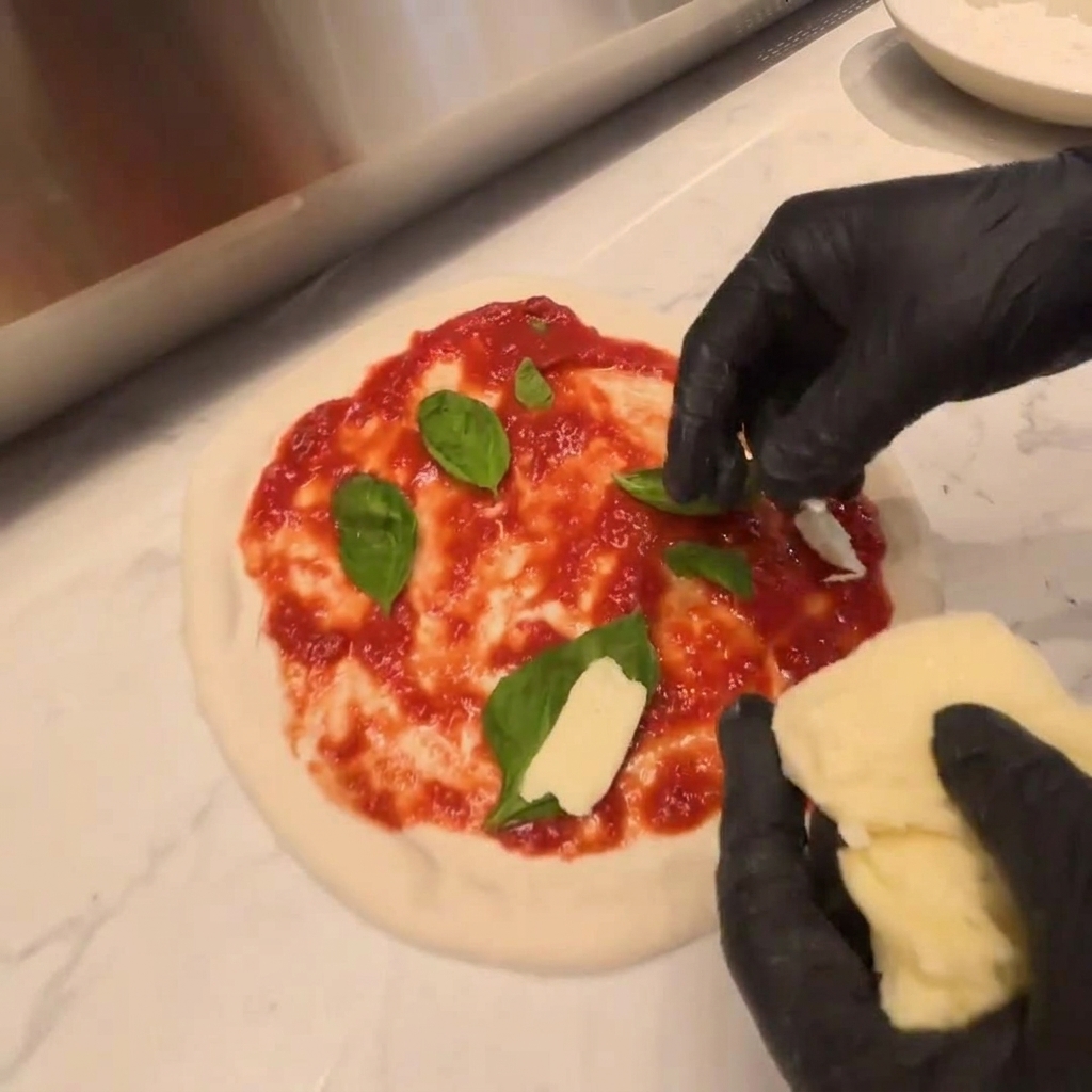 Kawałki świeżej mozzarelli układane na warstwie rukoli na surowym cieście do pizzy.
