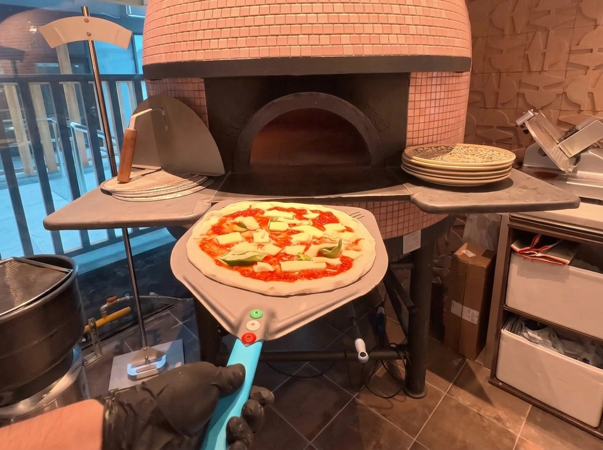 Pizza na metalowej łopacie wkładana do tradycyjnego pieca opalanego drewnem z cegły.