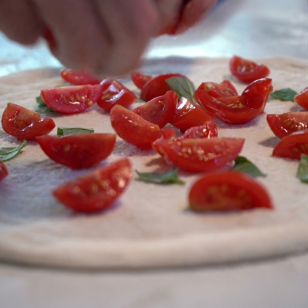 Sos pomidorowy i plastry świeżych pomidorów dodawane do surowego ciasta na pizzę.