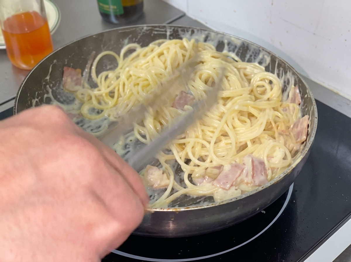 Ugotowany makaron spaghetti układany na patelni w kremowym sosie.